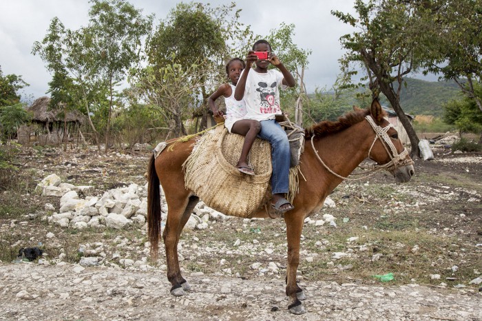 Two children sit atop a donkey taking a photo of the photographer